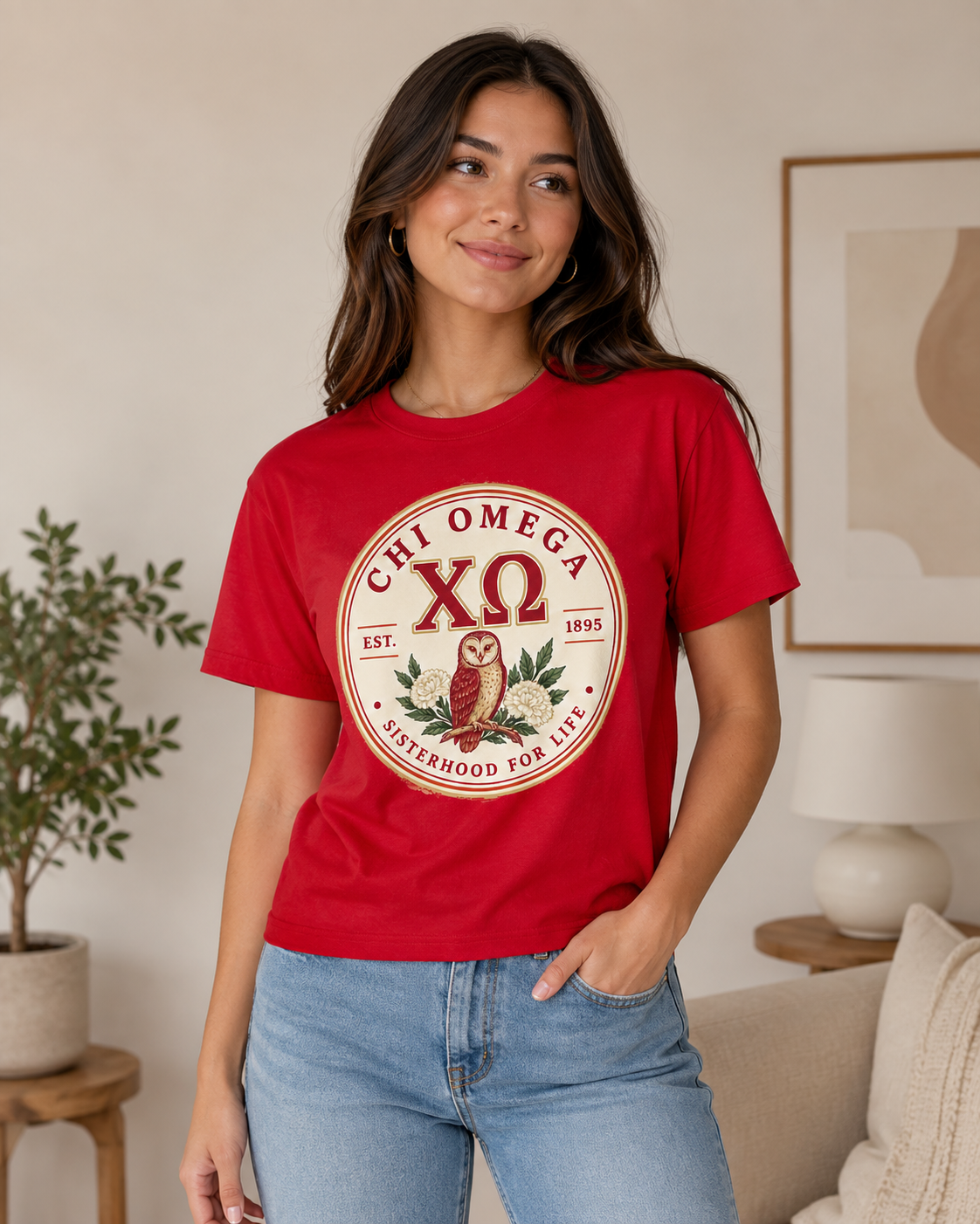 Woman wearing a red Chi Omega T-shirt with circular owl and floral sisterhood emblem indoors